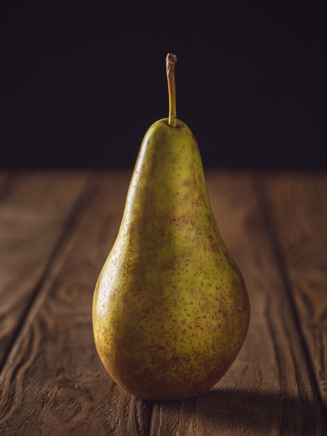 close-up shot of ripe yellow pear on rustic wooden table on black